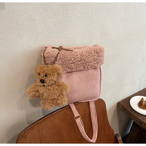 Borsa a secchiello rosa con bordo in peluche e ciondolo a forma di orsetto su una sedia