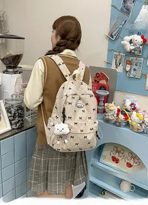 Detail of beige corduroy backpack featuring black bow prints and a white cloud plush charm