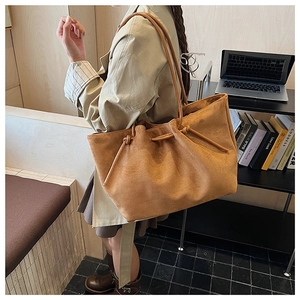 Detail of caramel suede tote bag with drawstring closure worn by a model in a trench coat