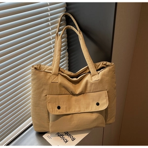 Detail of canvas tote bag showing front pocket with dual black snap buttons and straps