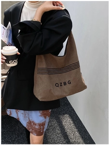 Detail of a large brown canvas shoulder bag with QZBG lettering on a stylish model