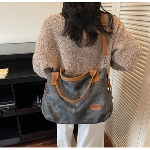 Detailed view of dark grey canvas tote bag with brown straps worn by a model indoors