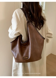 Detailed view of brown vintage leather shoulder bag with panted logo on trench coat
