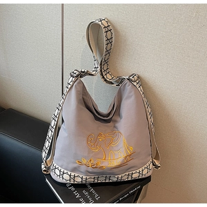 Close-up of golden elephant embroidery and woven shoulder strap on gray canvas bag