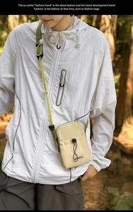 Détail du petit sac bandoulière beige avec sangle verte dans un décor de forêt