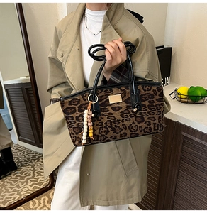 Detail of leopard print tote bag with black handles and gold logo worn with beige coat
