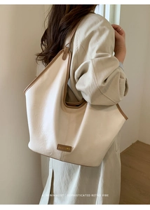 Detail view of large beige tote bag with brown trim and metal logo on a model