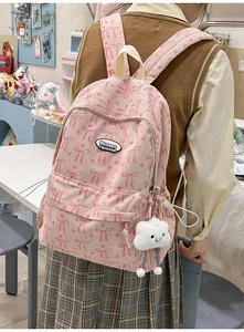 Close-up of pink corduroy backpack featuring red bow prints and a white plush charm