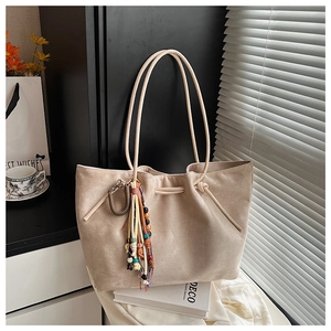 Detailed close-up of beige suede tote bag with decorative tassel and wooden beads