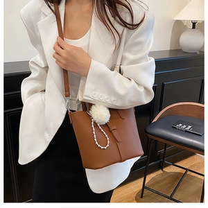 Dettaglio della borsa a secchiello in pelle marrone con pompon bianco e ciondolo di perle
