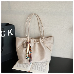 Detail of beige suede tote bag with colorful beaded charm and drawstring on book background