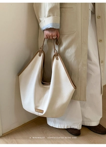 Detail of a large cream tote bag with brown trim and elegant brand logo on the front