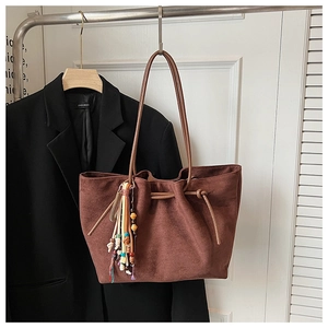Detail of suede tote bag featuring side drawstrings and a colorful beaded tassel charm