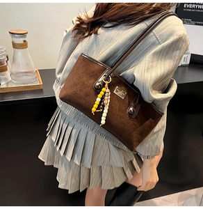 Detail of dark brown matte shoulder bag featuring beaded charms and metal brand plaque