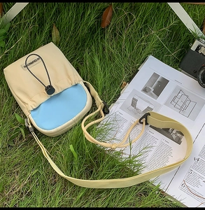 Détail d'un petit sac bandoulière beige et bleu à cordon sur l'herbe avec sangle