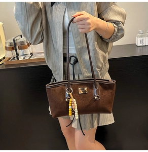Detailed shot of brown suede tote bag featuring a gold logo plaque and colorful tassel charm