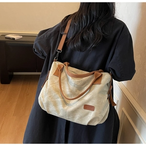 Detail of canvas tote bag with brown straps worn over a dark coat for daily commute