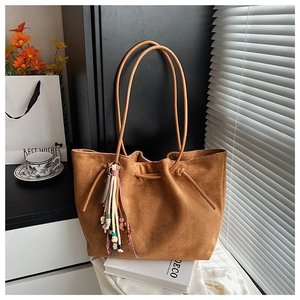 Detail of a brown suede tote bag with ethnic tassel charm and beaded decorative accents