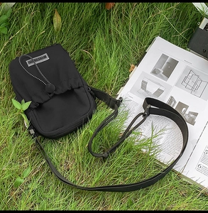 Détail d'un sac bandoulière en nylon noir avec cordon de serrage sur une pelouse