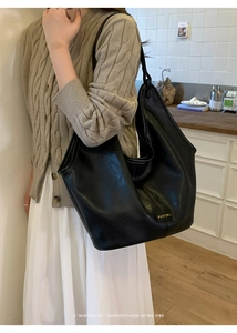 Detail of a large black leather tote bag featuring a metallic logo and vintage aesthetic