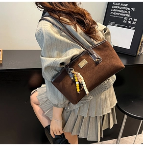 Close-up of brown suede tote bag featuring a metal nameplate and beaded fringe charm