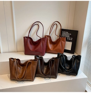Five assorted colors of large faux leather tote bags displayed in a minimalist setting