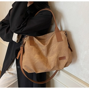 Detail view of large brown canvas tote bag with adjustable strap and leather logo patch
