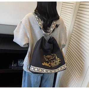 Detail of black nylon backpack featuring gold elephant embroidery and geometric strap design
