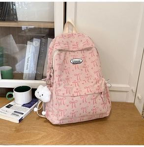 Pink corduroy backpack with bow prints and a white cloud plush charm in a cozy room