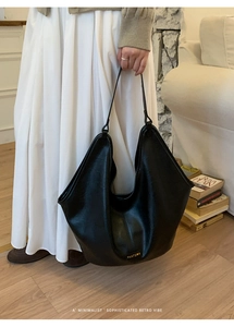 Detail of a minimalist black leather tote bag with gold brand lettering on soft hobo style