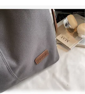 Close-up of grey canvas tote bag with brown leather brand tag and casual lifestyle decor