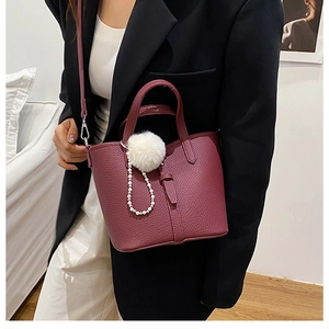 Dettaglio borsa a secchiello bordeaux scuro con trama litchi e ciondolo a perla elegante