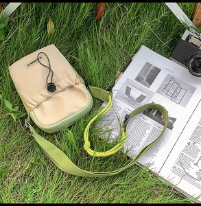 Petit sac bandoulière en nylon bicolore sur herbe avec appareil photo et magazine