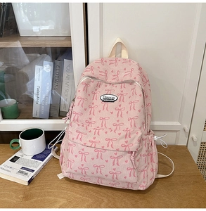 Pink corduroy backpack with bow detail and heart pattern on a wooden desk