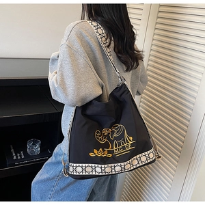 Detail of embroidered elephant pattern and geometric strap on a black canvas tote bag