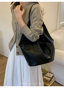 Side view of woman carrying a large black leather tote bag with elegant metal logo detail