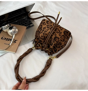 Sac seau léopard avec bandoulière tressée posé sur une table blanche avec magazines