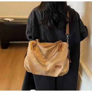 Detailed back view of a large brown canvas tote bag worn as a crossbody by a model