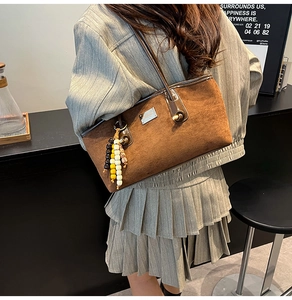Close-up of brown suede tote bag with boho bead charm and shiny dark handles