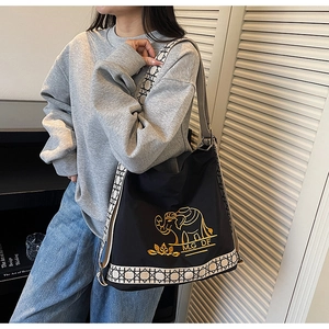 Detail of black canvas bucket bag featuring golden elephant embroidery and geometric strap