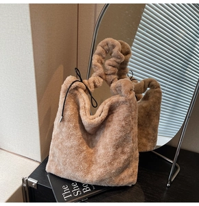 Detail view of camel plush tote bag with pleated handle and drawstring on a black table