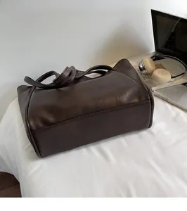 Brown leather tote bag next to a laptop and book on a white fabric surface