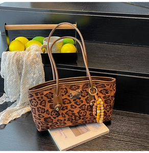 Detail of leopard print tote with leather strap, gold logo and beaded charm on stairs