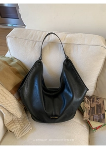 Detail of black pebbled leather tote bag with gold logo on a cozy beige sofa