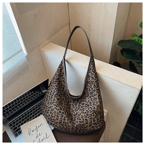 Leopard print tote bag with brown shoulder strap on a wooden desk with laptop