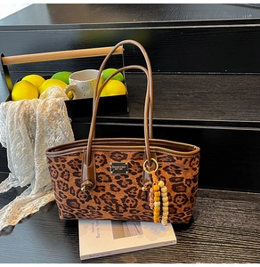 Detail of leopard print tote bag with brown handles and silver logo on a wooden background