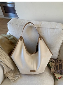 Detail of cream hobo tote bag with brown trim on a cozy sofa setting