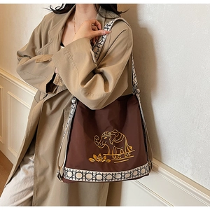 Close-up of golden elephant embroidery and geometric strap on a brown canvas tote bag