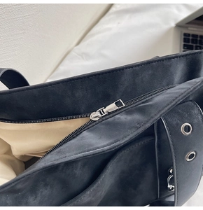 Detail of black suede tote bag with silver zipper closure and metal eyelet accents