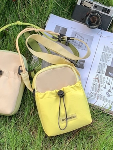 Mini sacs bandoulière en nylon jaune et vert présentés sur de l'herbe fraîche